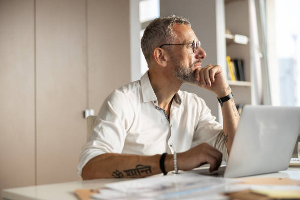 Thoughtful entrepreneur is staring in the window Philosophical person propping up his chin with a hand and getting distracted from working process with something outside mesmerised stock pictures, royalty-free photos & images