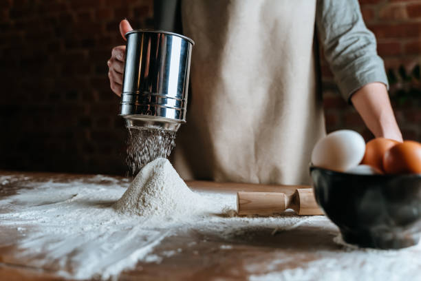 feche a mulher chef padaria peneirando farinha de peneira sobre a mesa, preparando-se para fazer pão caseiro - sifting - fotografias e filmes do acervo