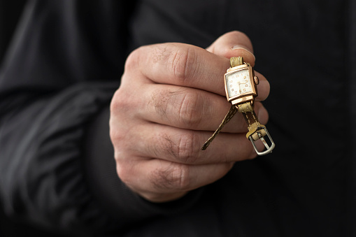 Male hand holding an old gold wristwatch. Illegal antiquities trade concept.