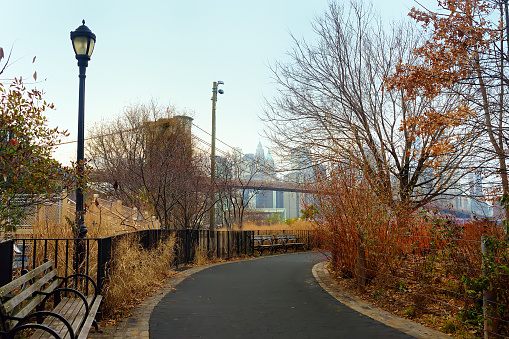 Alley of Main Street Park on the background of famous Brooklyn bridge in New York in winter day. Parks of NYC.