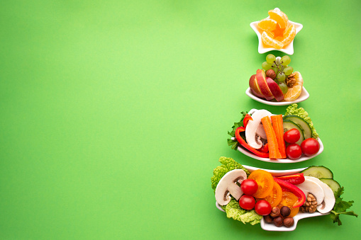 Plate in the form of a Christmas tree with vegetables, fruits, mushrooms and berries.Green background. The concept of vegetarian treats for the holiday. Copy space.