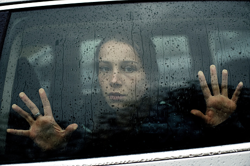 Sad woman looking through a wet car window