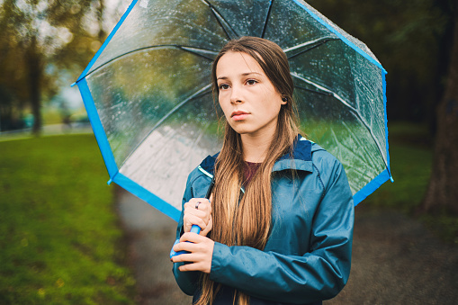 Sad young woman with umbrella standing in the autumn rain
