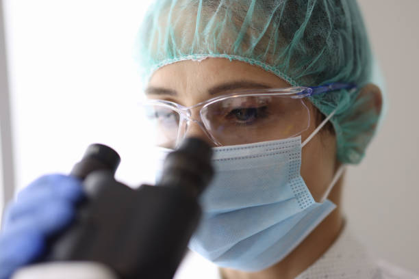 istock Researcher wearing mask and glasses looks through microscope. 1283918017