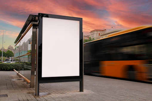 Bus stop with blank billboard, with blurred motion bus at sunset