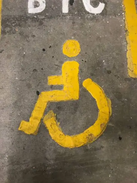 a Sign of a yellow person and wheelchair on the floor in a parkinglot