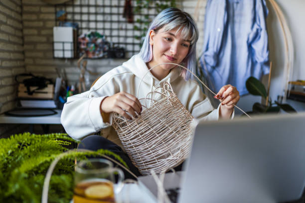 joven azul pelo mujer tejer una olla de mimbre en casa usando portátil para ver tutorial en línea - craft project fotografías e imágenes de stock