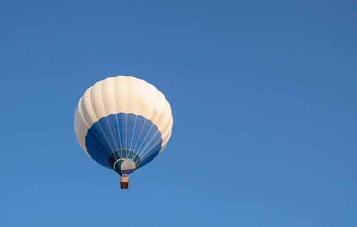 Blue and white hot air balloon flying in blue sky with room for text.