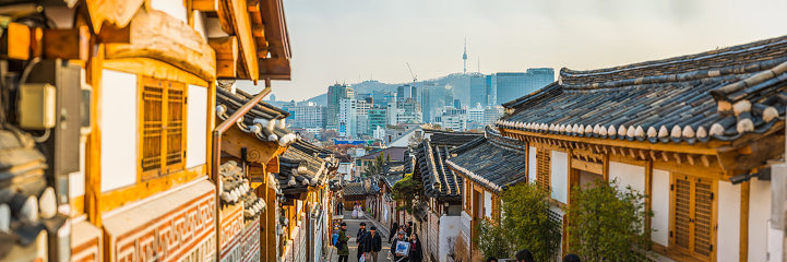 The iconic spire of Namsan Tower overlooking tourists visiting the traditional wooden homes of Bukchon Hanok village in Seoul, South Korea’s vibrant capital city.