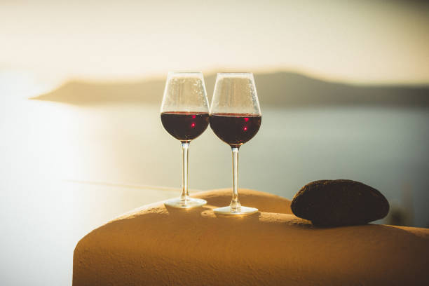 Wine glasses with red wine at sunset, view from idyllic village Firostefani on Santorini island, Greece. Property released.