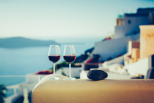 Wine glasses with red wine at sunset, view from idyllic village Firostefani on Santorini island, Greece. Property released.