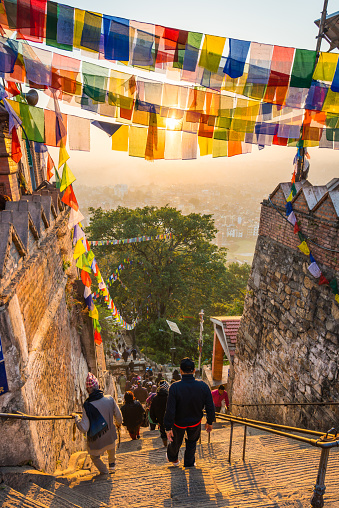 Brightly coloured Buddhist prayer flags glowing at sunrise as pilgrims walk the steep steps to Swayambhunath monkey temple over kathmandu, Nepal's vibrant capital city.