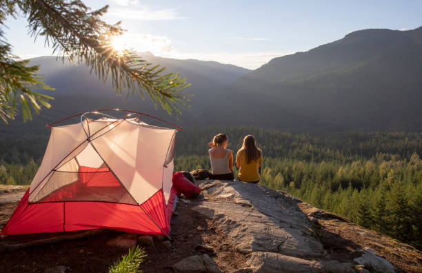 Young women watch the sunset on a mountain ledge campsite stock photo