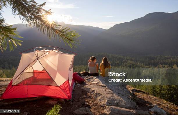 Young Women Watch The Sunset On A Mountain Ledge Campsite Stock Photo - Download Image Now