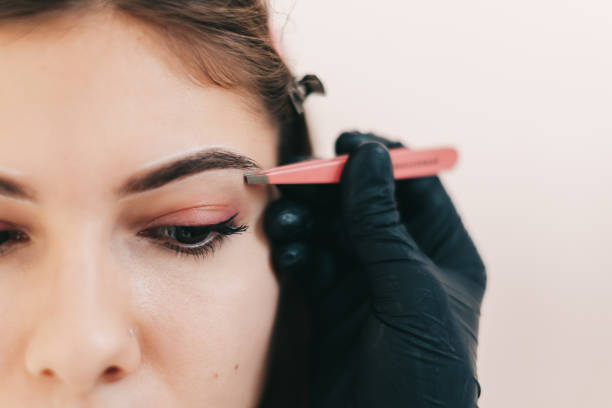 istock Eyebrow shaping procedure, make-up master uses tweezers to shape the eyebrows. 1283936375