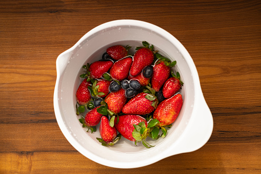 Image of strawberries and blueberries soaked in a bowl with water, vinegar and baking soda on a simple cleaning process preventing from any diseases and virus infections