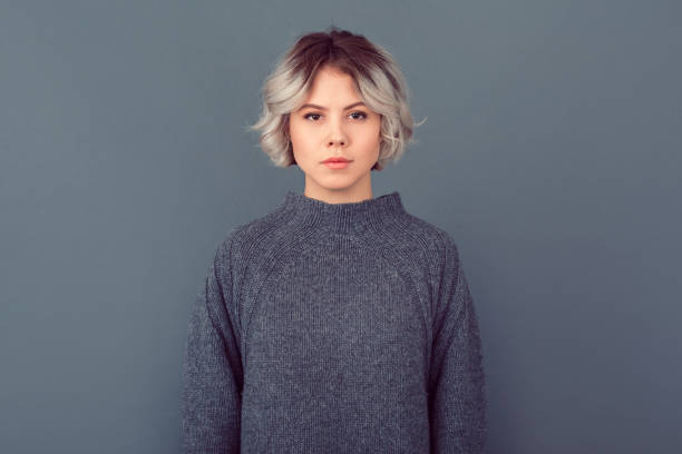 Young woman in a grey sweater studio picture isolated on grey background serious stock photo
