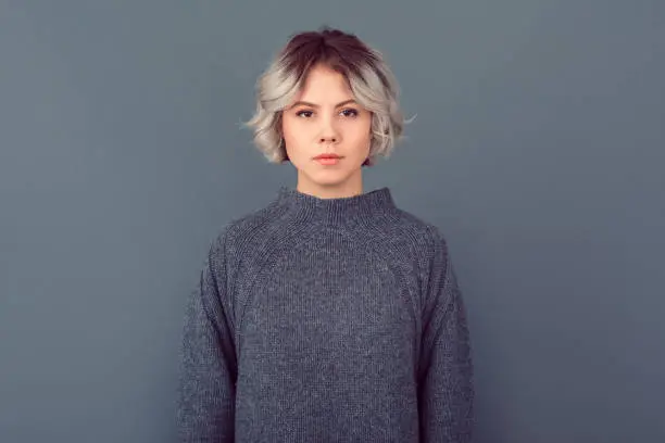 Photo of Young woman in a grey sweater studio picture isolated on grey background serious