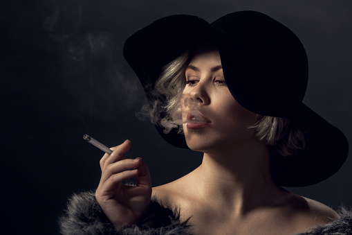 Young woman luxury style isolated wearing fur coat and hat smoking looking at smoke thinking close-up