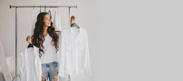 beautiful young woman stylist standing near rack with hangers with white clothes. shopaholic with many clothes. - lifestyles designer store luxury imagens e fotografias de stock