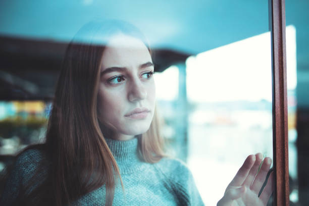 sad lonely young woman looking thoughtfully through window Causian sad lonely young woman looking thoughtfully through the window during pandemic, and celebrating christmas alone, shot with canon 5dsr skeptical look stock pictures, royalty-free photos & images