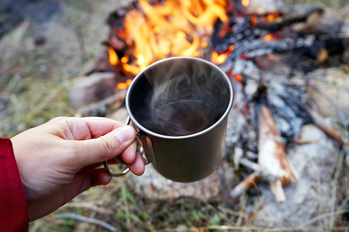 Hand holding a mug of hot cocoa over a campfire