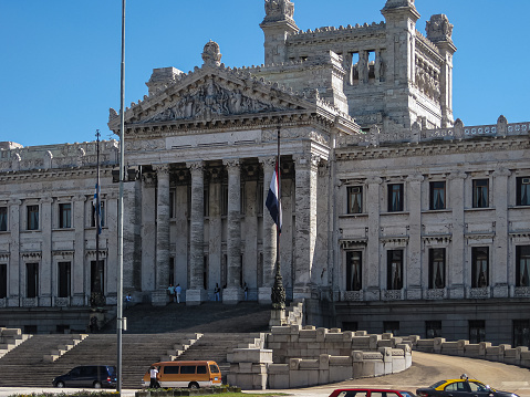 Montevideo, Uruguay- December 18, 2008: Legislative Palace or parliament is gray stone monumental building showing statues, entrance, facades, and stairways up under blue sky. Cars in front.