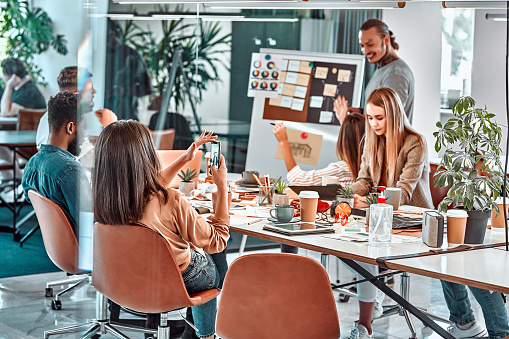 Reunión en la oficina, equipo productivo de jóvenes profesionales que trabajan en una gran mesa utilizando dispositivos tecnológicos modernos. photo