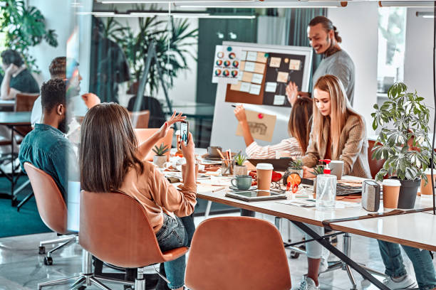 réunion au bureau, équipe productive de jeunes professionnels travaillant à une grande table à l’aide d’appareils technologiques modernes. - coworking photos et images de collection