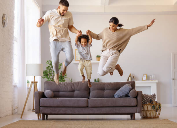 família diversificada brincando perto do sofá - domestic life jumping child sofa - fotografias e filmes do acervo