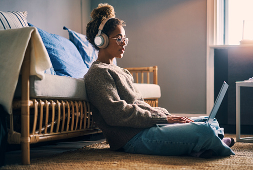 Shot of a young woman wearing headphones while using a laptop at home