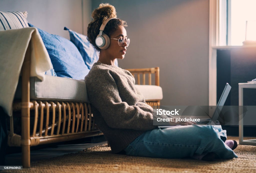 Music keeps her productive Shot of a young woman wearing headphones while using a laptop at home Downloading Stock Photo