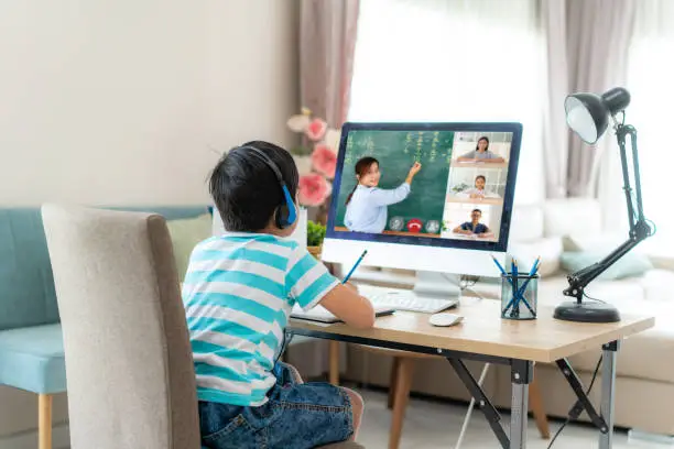 Asian boy student video conference e-learning with teacher and classmates on computer in living room at home. Homeschooling and distance learning ,online ,education and internet.