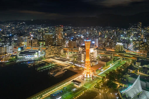 Kobe, Japan - November, 27th 2018: Glowing Kobe Port Waterfront Cityscape and Harbor View with gfamous orange illuminated Kobe Port Tower at Night. Aerial Drone Point of View over the City of Kobe. Kobe, Honshu, Japan, Eastern Asia, Asia