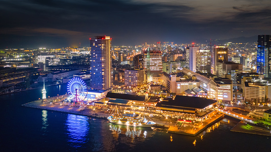 Kobe, Japan - November, 27th 2018: Kobe Cityscape Harbor Waterfront Panorama at Night. Aerial Drone Point of View Panorama. Illuminated Skyscrapers and the glowing urban sprawl view from the seaside, Kobe, Hyogo Prefecture, Honshu, Japan, Asia.