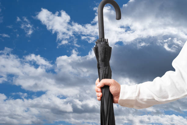 istock Man holding closed black umbrella on blue cloudy sky background 1283990464