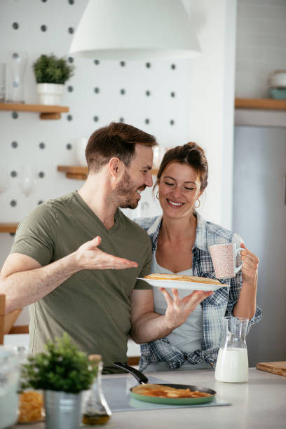 Husband and wife making pancakes at home.