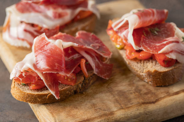 Wooden try with toasted brad slice with fresh tomatoes and cured ham. Delicious appetiser Italian prosciutto and Spanish Iberian ham snack Wooden try with toasted brad slice with fresh tomatoes and cured ham. Delicious appetiser Italian prosciutto and Spanish Iberian ham snack appetiser stock pictures, royalty-free photos & images