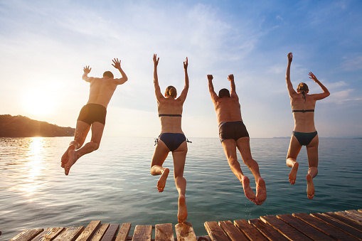 group of friends jumping to the sea from the pier, happy beach holidays
