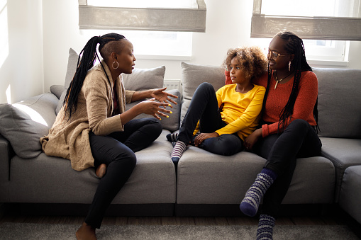 Three female members of an African American family sitting on the sofa and talking some funny stories.