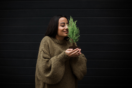 A girl enjoys the smell of an evergreen plant she is holding in her palms.