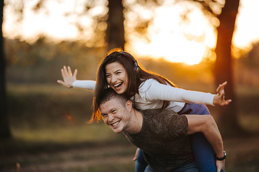 Cheerful young couple enjoying picnic day in nature at sunset, having fun together while piggybacking
