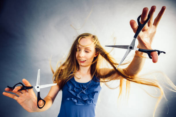 Haircut coiffure haircare concept. Crazy girl with blowing long blonde hair holding scissors, showing work tools normal and thinning shears