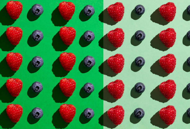 Above view of Over flowing white bowl of blueberries with a single raspberry on top on yellow background.