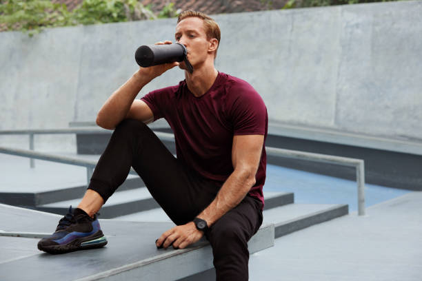 istock Young Man Drinking From Bottle After Intense Workout On Concrete Steps. Handsome Caucasian Sportsman With Strong Muscular Body In Fashion Sportswear Having Break. 1284014733