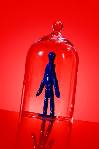 a blue articulated doll in a glass bell jar on a red background