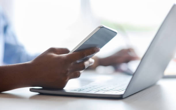 istock Unrecognizable black woman using smartphone and working on laptop in office, closeup 1284016381