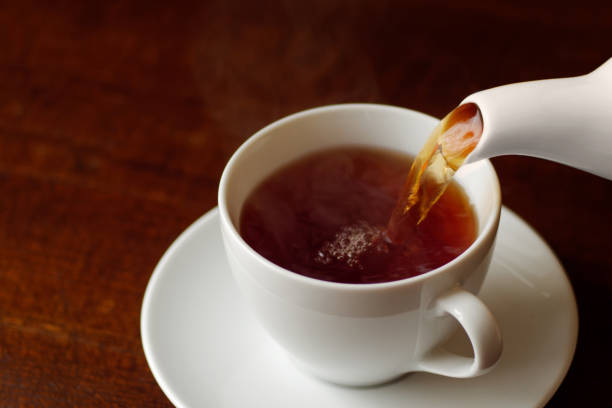 istock Black tea with steam poured into white cup on saucer from a pot. 1284017526
