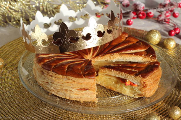 Epiphany kings cake with a golden paper crown and one small porcelain good luck charm inside. Galette des rois. Epiphany cake with a golden paper crown and one small porcelain  charm inside on a glass plate on the holiday table. Slice of kings cake. Galette des rois. galette stock pictures, royalty-free photos & images