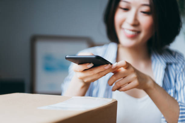 Young Asian woman receiving a parcel by home delivery service and scanning QR code with smartphone Young Asian woman receiving a parcel by home delivery service and scanning QR code with a smartphone scanning activity photos stock pictures, royalty-free photos & images
